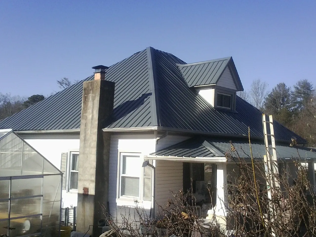 Dark blue standing seam metal roof on a white farmhouse with dormer — Slate & Tile Roof Repair by Roofing Brothers in Fort Smith