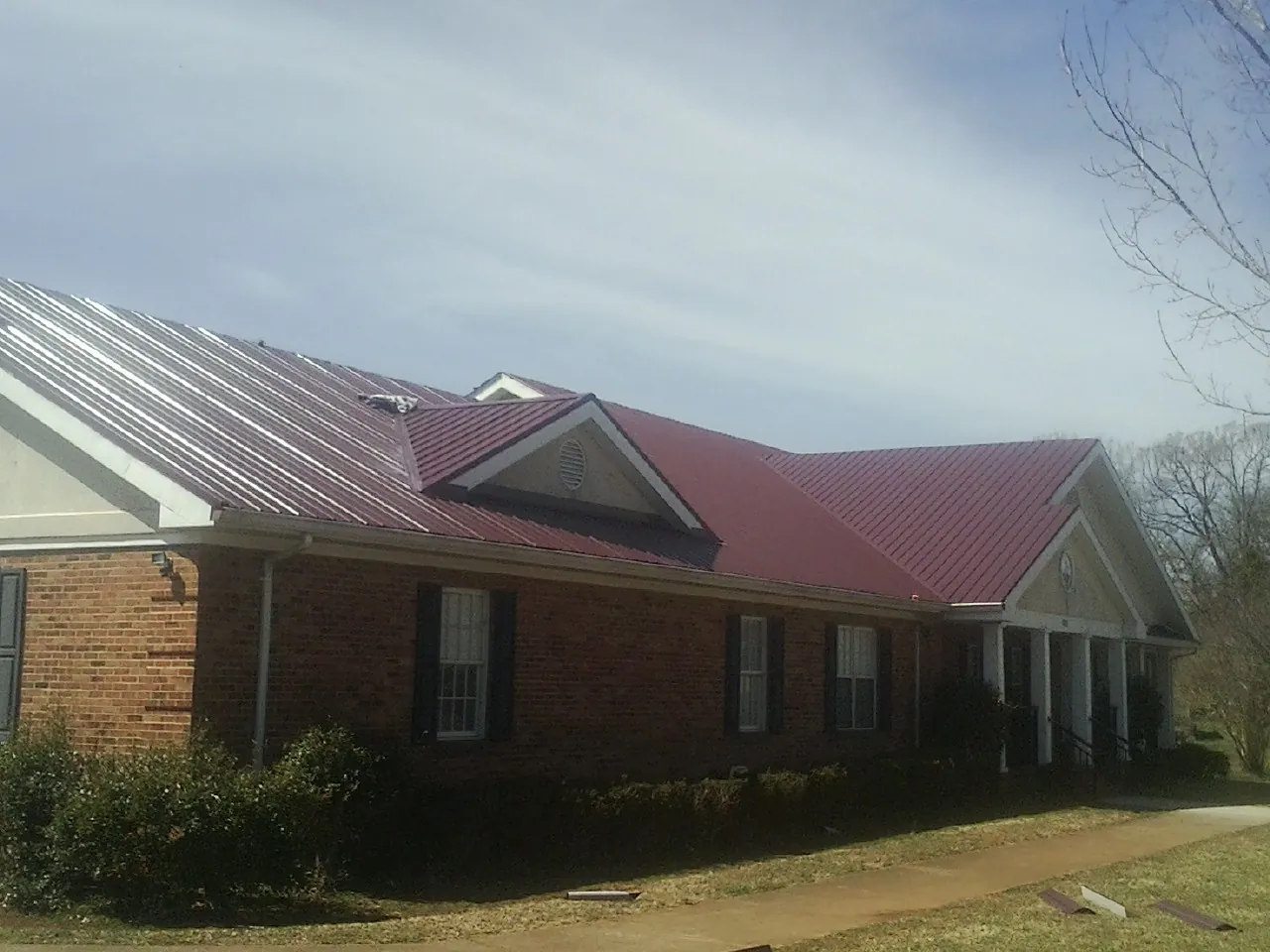 Red metal roof with gabled entries on a long brick building, from a Hail Damage Roof Repair job in Fort Smith