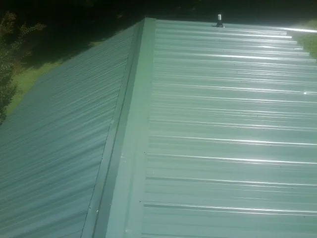 New green metal panels meeting at the ridge of a roof — Flat Roof Repair work by our crew in Fort Smith