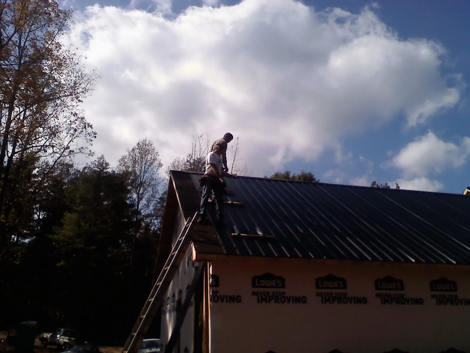 Roofer fastening dark metal panels high against a cloudy sky, from a Roof Inspection job in Fort Smith