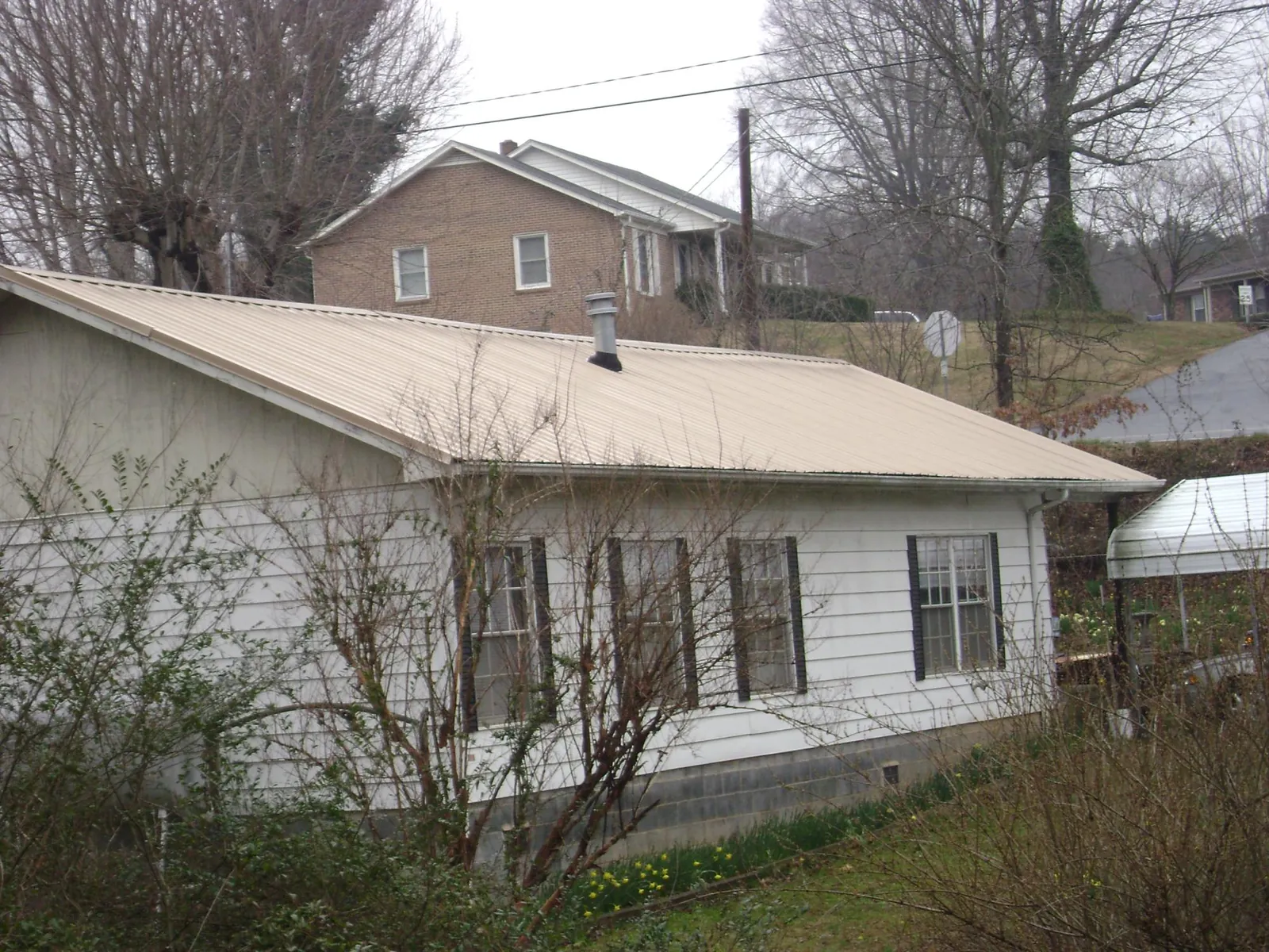 Tan metal roof on a white sided house set into a hillside — Commercial Roofing by Roofing Brothers in Fort Smith