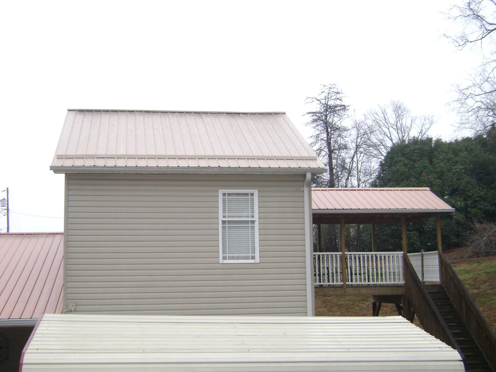 Tan metal roofs on a two story addition and attached porch, from a Roof Replacement job in Fort Smith